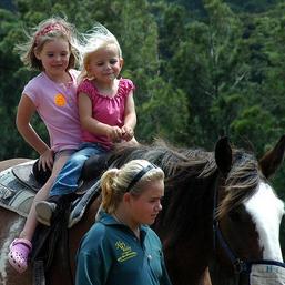 Two girls riding a horse and one girl walking beside the horse