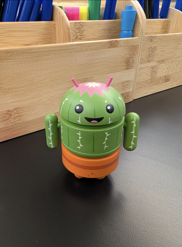 Un piccolo robot Android verde con un design simile a un cactus è seduto su
             una superficie nera.